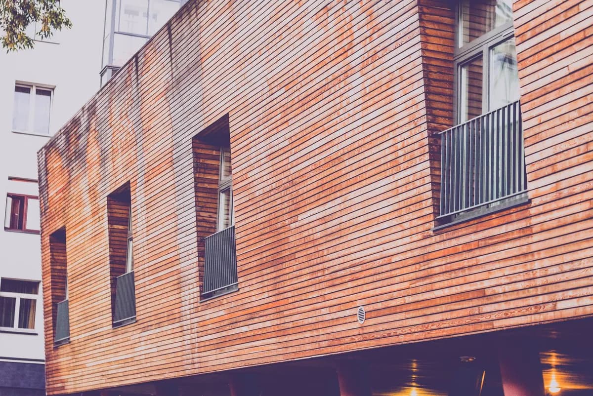 Contemporary wooden facade of a residential building with windows and railings, showcasing urban architecture.