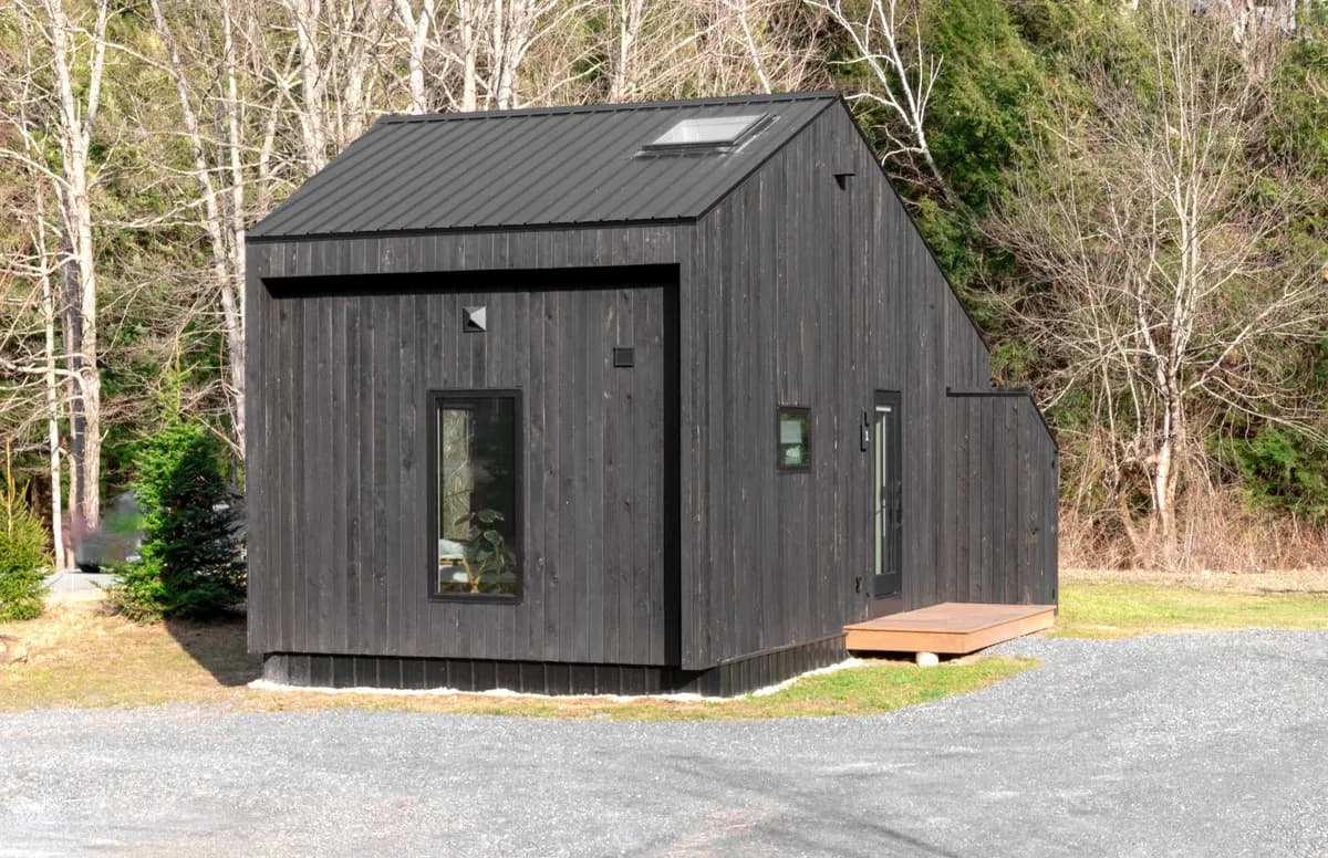 A minimalistic black tiny house nestled in a forest area, showcasing sustainable living.
